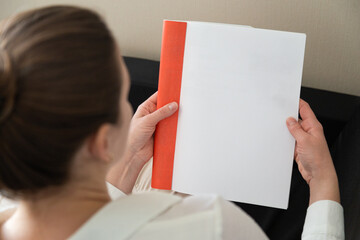 Beautiful female hands hold an open book or magazine in a room on a black sofa