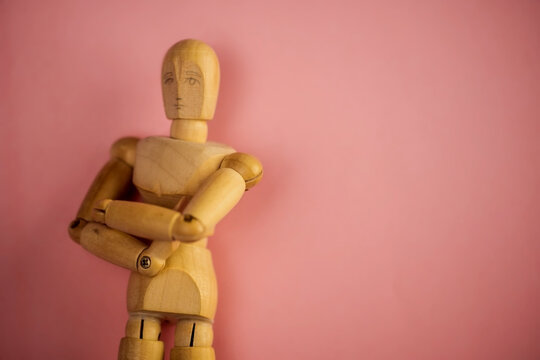 wooden dummy doll with crossed arms on pink background.