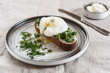 Healthy Breakfast with Poached Egg on toast with cream cheese and chopped mix of green onions, dill and parsley on greige linen tablecloth