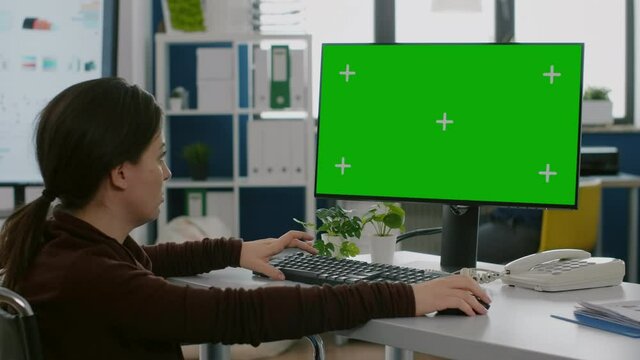 Disabled handicapped worker immobilized in wheelchair looking at computer with green screen chroma key mock up isolated display typing financial statistics, working in start up company office