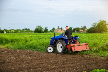 A farmer with a cultivation unit on a tractor rides to cultivate a field. Milling soil, crushing...