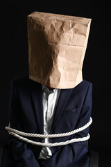 Male hostage with paper bag on dark background