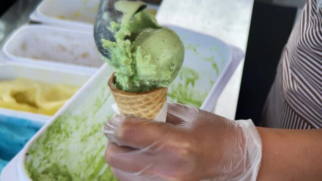An ice cream maker puts a ball of pistachio ice cream into a waffle cone. High quality 4k footage