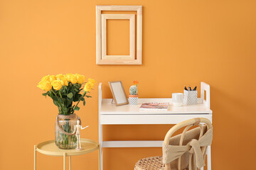 Stylish workplace and vase with yellow roses near color wall