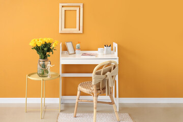 Stylish workplace and vase with yellow roses near color wall