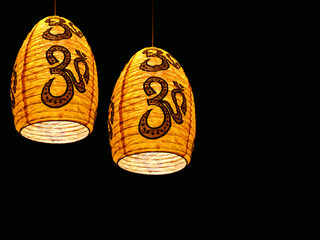decorative hanging paper lanterns on black background. om symbols background. Asian-style white rice paper lamp lit with a yellow bulb, interior decoration.