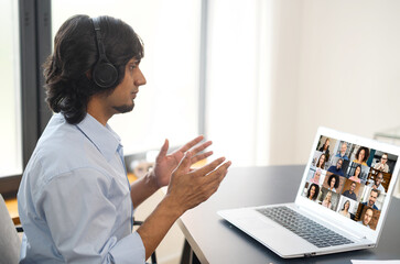 Young indian man using computer app for video communication, talking online with a group of diverse international people, male employee involved video meeting with multiracial colleagues