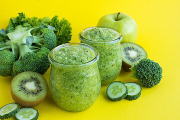 Green smoothie or puree in the small glass jars on the yellow background. Close-up.
