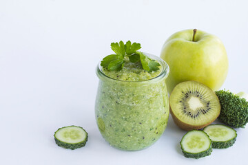 Green smoothie or puree in the small glass jar on the white background. Close-up. Copy space.
