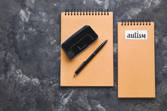 Notebooks with word AUTISM and pen on grunge background