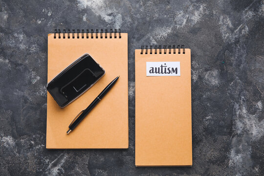 Notebooks with word AUTISM and pen on grunge background
