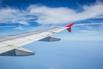 Wing of airplane flying above the clouds in the blue sky.