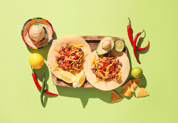 Board with tasty tacos and sombrero on color background