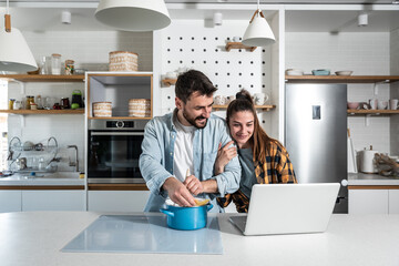 Obraz premium Young couple man and woman cooking spaghetti pasta for dinner at their home while looking recipes online and listening to the instruction from online cook