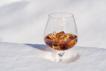 Glass of cognac with ice on a bed of snow and white background, close up