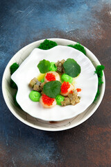 Scallops with caviar, microgreens and green sauce on a white plate.