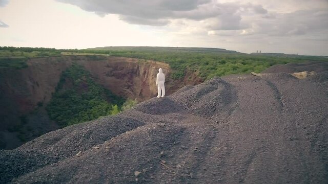 a man in a white bacteriological protective suit looks at a huge hole in the ground. Panorama. Drone shooting