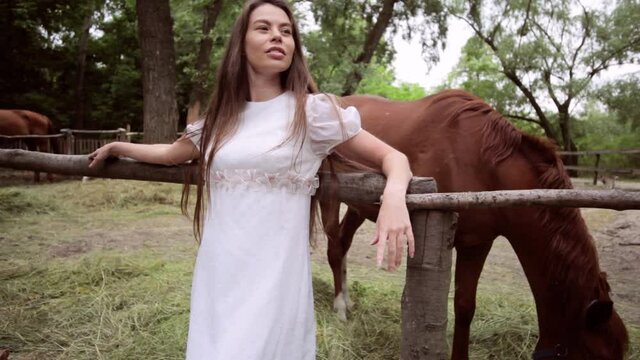 Beautiful woman on the background of a grazing horse at the ranch.