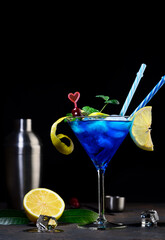 Blue lagoon cocktail with blue curacao liqueur, vodka, lemon juice and soda. Blue cocktail in martini glasses on black background