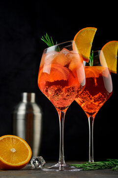 Wineglass of ice cold Aperol spritz cocktail served in a wine glass, decorated with slices of orange and rosemary branch. Black background