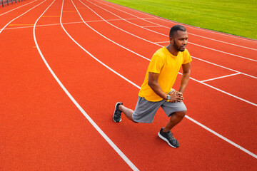 Obraz premium Portrait of sporty focused black man in sports wear warming up before training outdoors, wearing yellow trendy sportswear.Young Afro American stretching body at the stadium field