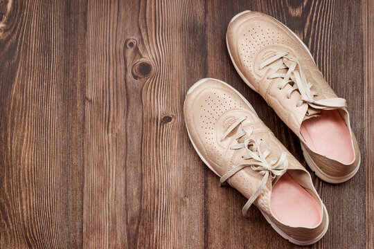 Empty space for text. A pair of women's summer sports shoes in gold color on a brown wooden background