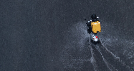 Delivery service from cafes and restaurants, courier on a scooter with a yellow backpack traveling through the puddles. The courier delivers food on a motorcycle. Fast food delivery to customers