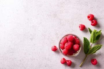 Fresh and ripe raspberries in a jar and fresh green sprig of mint on grey countertop