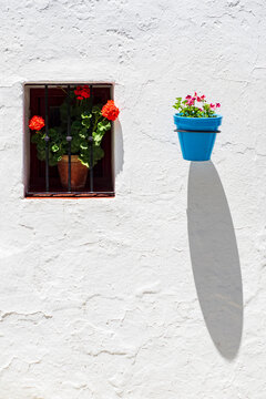 Maceta de color azul con flores junto a una ventana con geranios