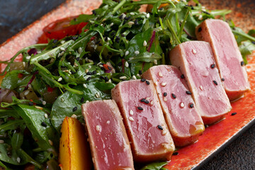 Fried tuna in slices with fresh tomatoes, sesame seeds and arugula salad