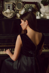 Young attractive lady is posing near piano, wearing black dress. Elegance