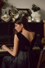 Obraz na płótnie Canvas Young attractive lady is posing near piano, wearing black dress. Elegance