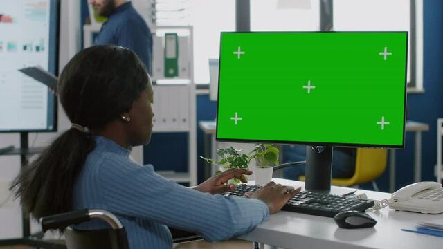 African disabled invalid handicapped businesswoman sitting in wheelchair analysing financial statistics, looking at pc with green screen chroma key mock up izolated desktop planning business project