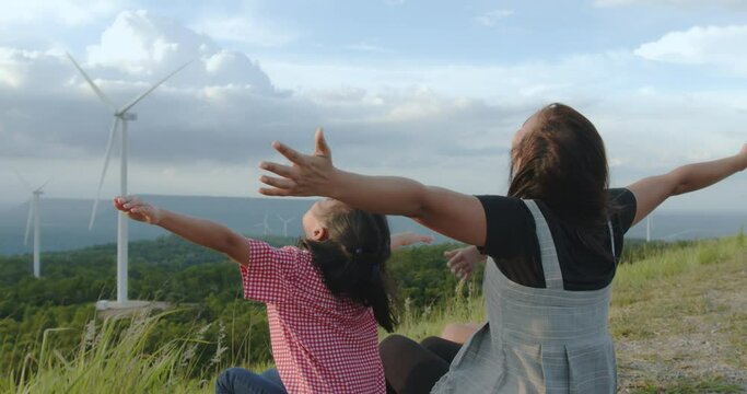 Asian child girl and mother raised their hands to fly and playing in the wind turbine field with fun together in slow motion shot