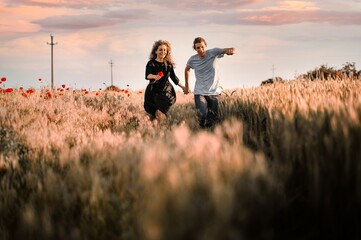 Woman and man running in wheat field at sunset