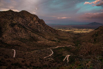 Aerial panoramic view of mountain ridges in Arizona and a valley with a dark blue and purple sky and clouds and a roadway up.