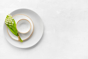 Beautiful lily-of-the-valley flowers and plates on light background