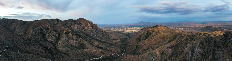 Aerial panoramic view of mountain ridges in Arizona and a valley with a dark blue sky and clouds and a roadway up.
