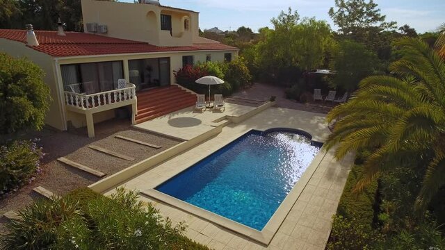 Traditional European villa with pool, solar panel and well-kept garden, aerial view from the sky. With tropical trees, palms