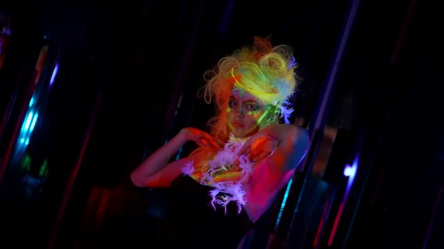 go-go dancer woman with fluorescent makeup on face and body is dancing in nightclub, medium portrait in darkness