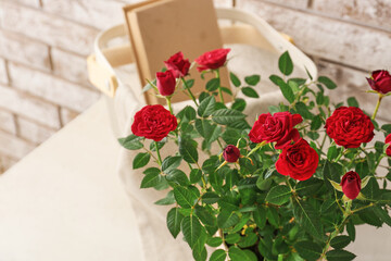 Obraz na płótnie Canvas Beautiful red roses in pot and basket with book on table near brick wall