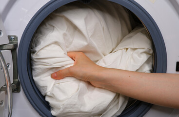 The girl puts white linen in the washing machine.