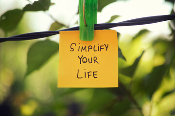 A yellow paper note with the phrase Simplify Your Life written on it hanging on a clothesline