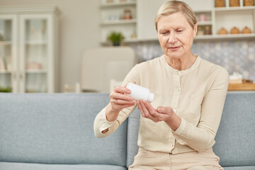 Senior woman sit on couch having daily vitamins or diet supplements at home, mature old female pensioner take dose of pills from meds bottle, elderly healthcare, medication concept