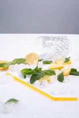 spilled glass of refreshing summer cocktail with ice, lemon and mint on white background