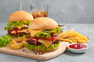 Burger with beef, cheese, sauce, pickles and French fries on a gray background.