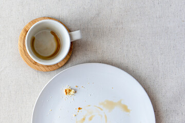 Table covered by tablecloth with coffee cup for espresso, plate with crumbs of dessert, top view, flat lay