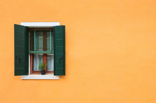 Window with green shutters on the yellow wall of the house. Colorful architecture in Burano island, Venice, Italy.
