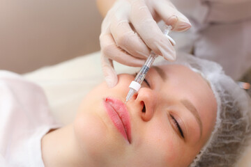 The girl is undergoing a lip augmentation procedure with a master cosmetologist who holds the lip edge with one finger and gives an injection of hyaluronic acid