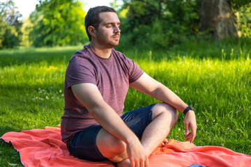 Photo of a young and attractive man sitting on a towel with his eyes closed and his legs crossed meditating in the middle of nature. Enjoying silence, relaxing with a guided meditation
